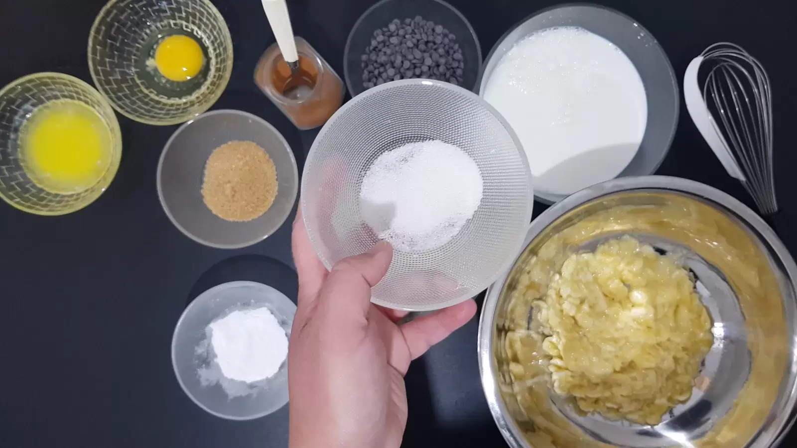 Bowl with baking powder, bowl with chocolate chips, cinnamon and spoon, bowl with egg, bowl with butter, bowl with brown sugar, bowl with oats, bowl with milk, bowl with vanilla sugar, bowl with baking powder, fork, whisk , mashed bananas in a bowl