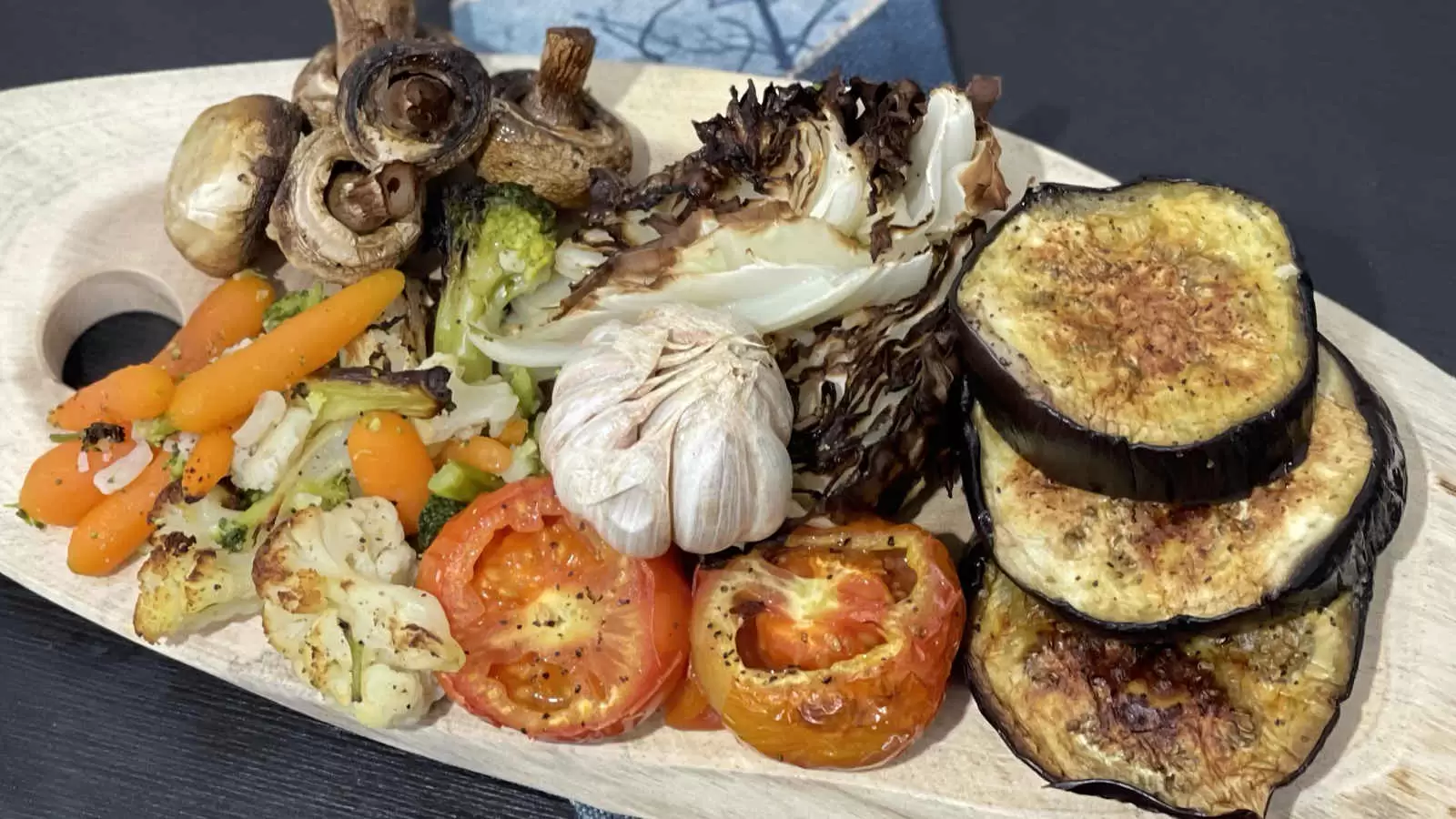 Eggplant mushrooms tomatoes cabbage carrots and  more roasted vegetables on a wooden tray