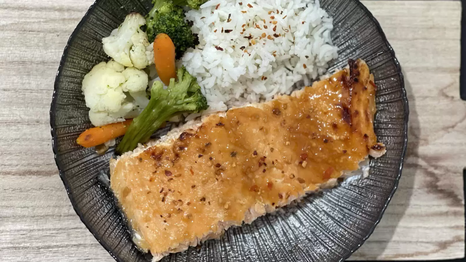 Baking Honey Glazed Salmon rice carrots broccoli and cauliflower on a black plate on a wooden board