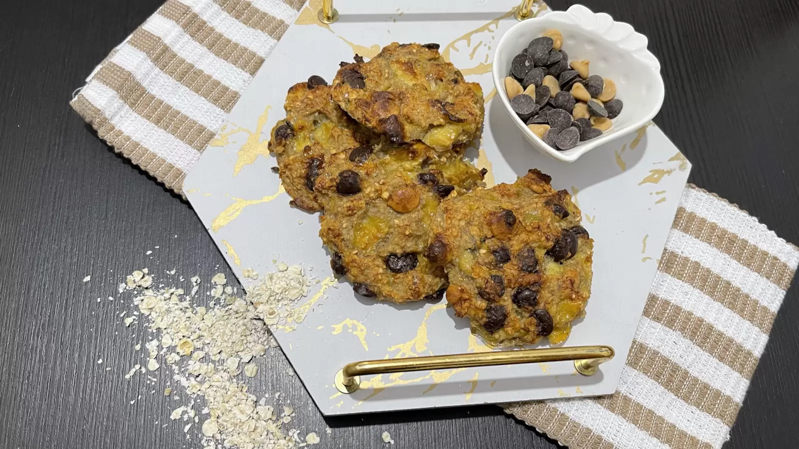 Banana and oatmeal cookies dish on a tray a bowl of chocolate chips oatmeal scattered on the table