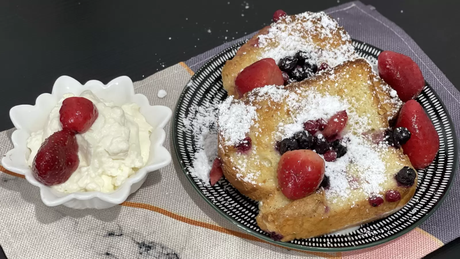 Berry Bread Pudding on a plate next to vanilla cream with strawberries in a bowl on a table