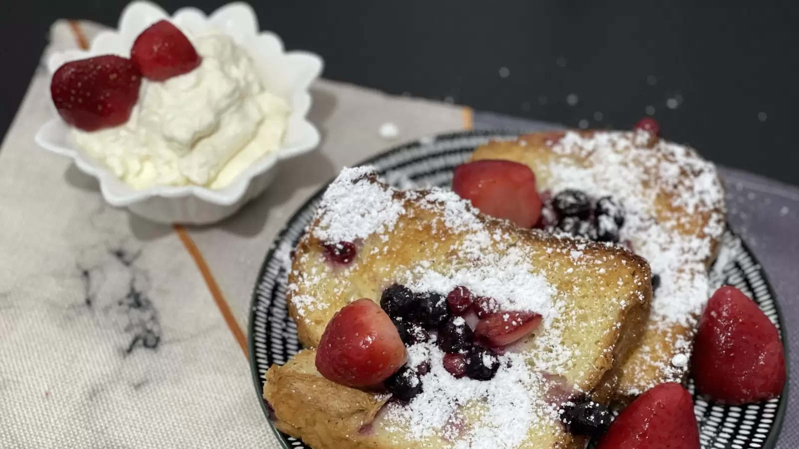 Berry Bread Pudding on a plate next to vanilla cream with strawberries in a bowl on a table