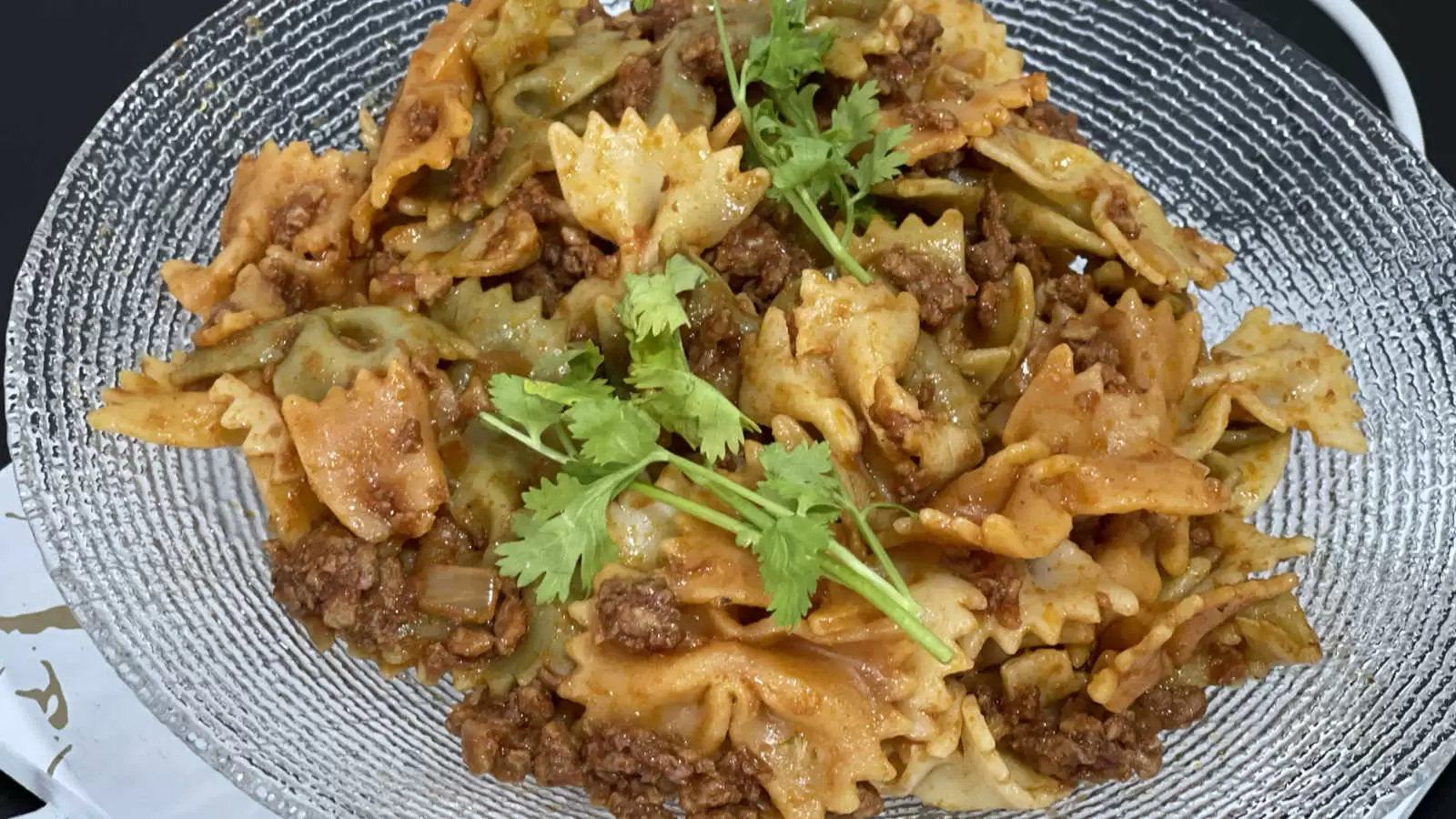 Farfalle with Bolognese meal on a plate on a black background