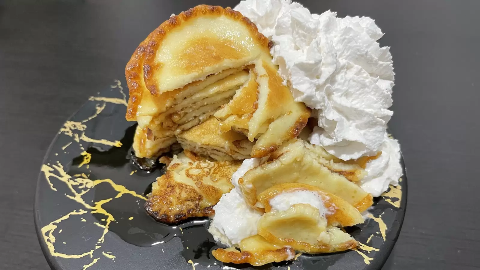Cheese pancakes for breakfast whipped cream on a black surface next to a towel with a fork and knife on a black table