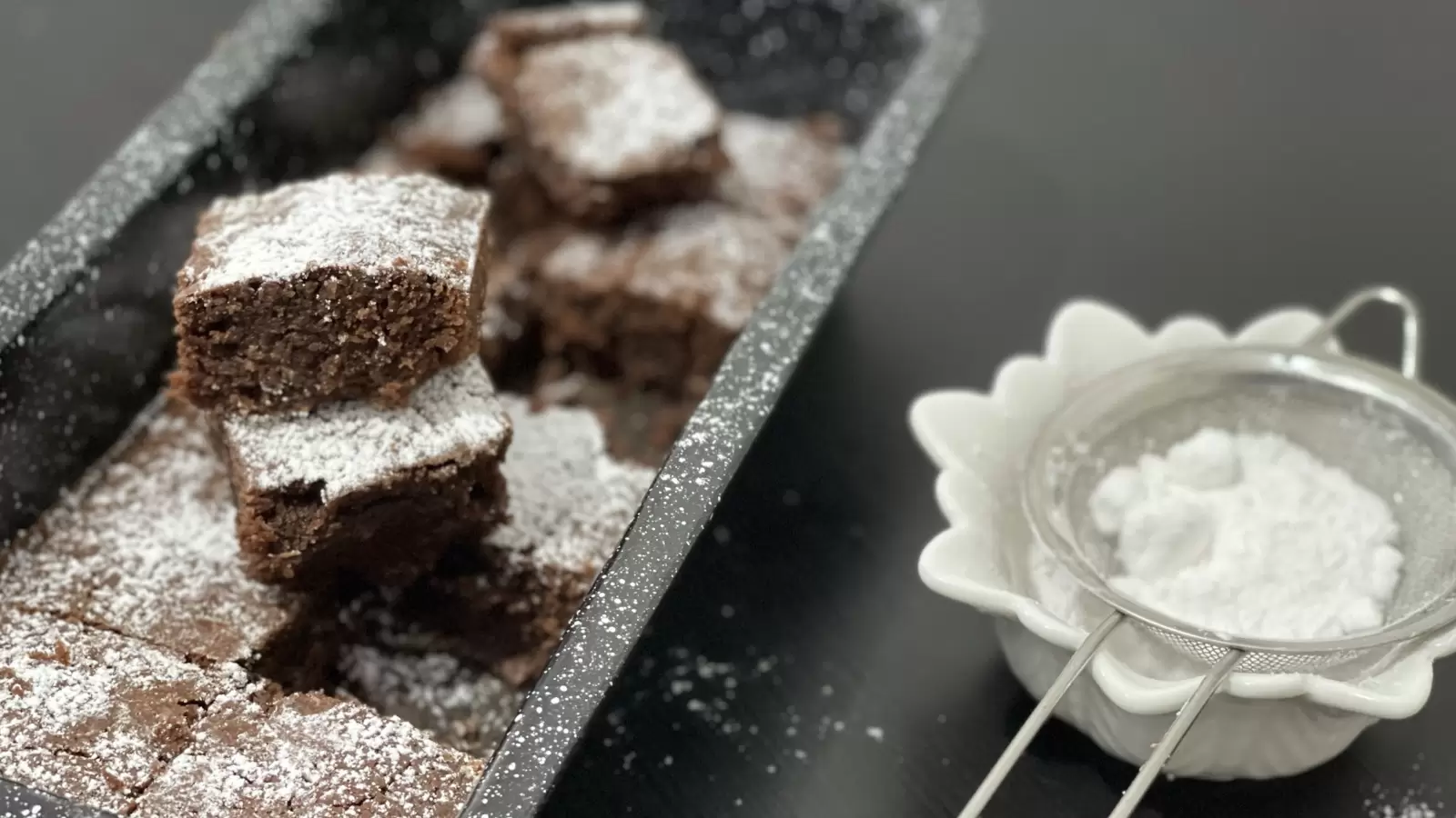 Brownies dish in a pan brownie pieces one on top of the other next to powdered sugar in a bowl