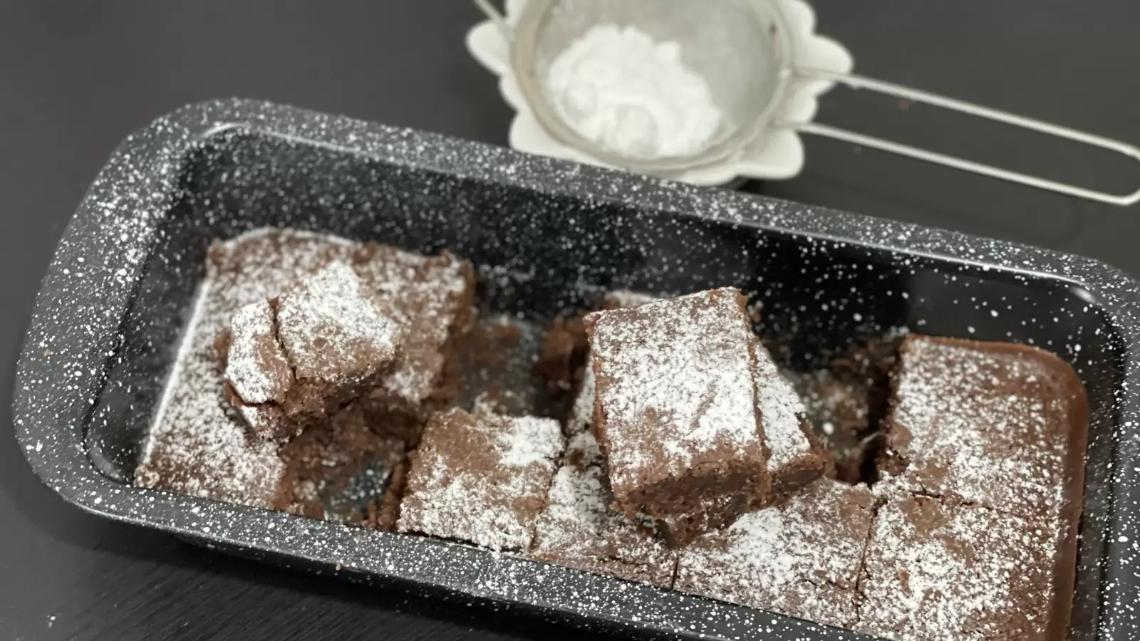 Brownies recipe in a pan brownie pieces one on top of the other next to powdered sugar in a bowl