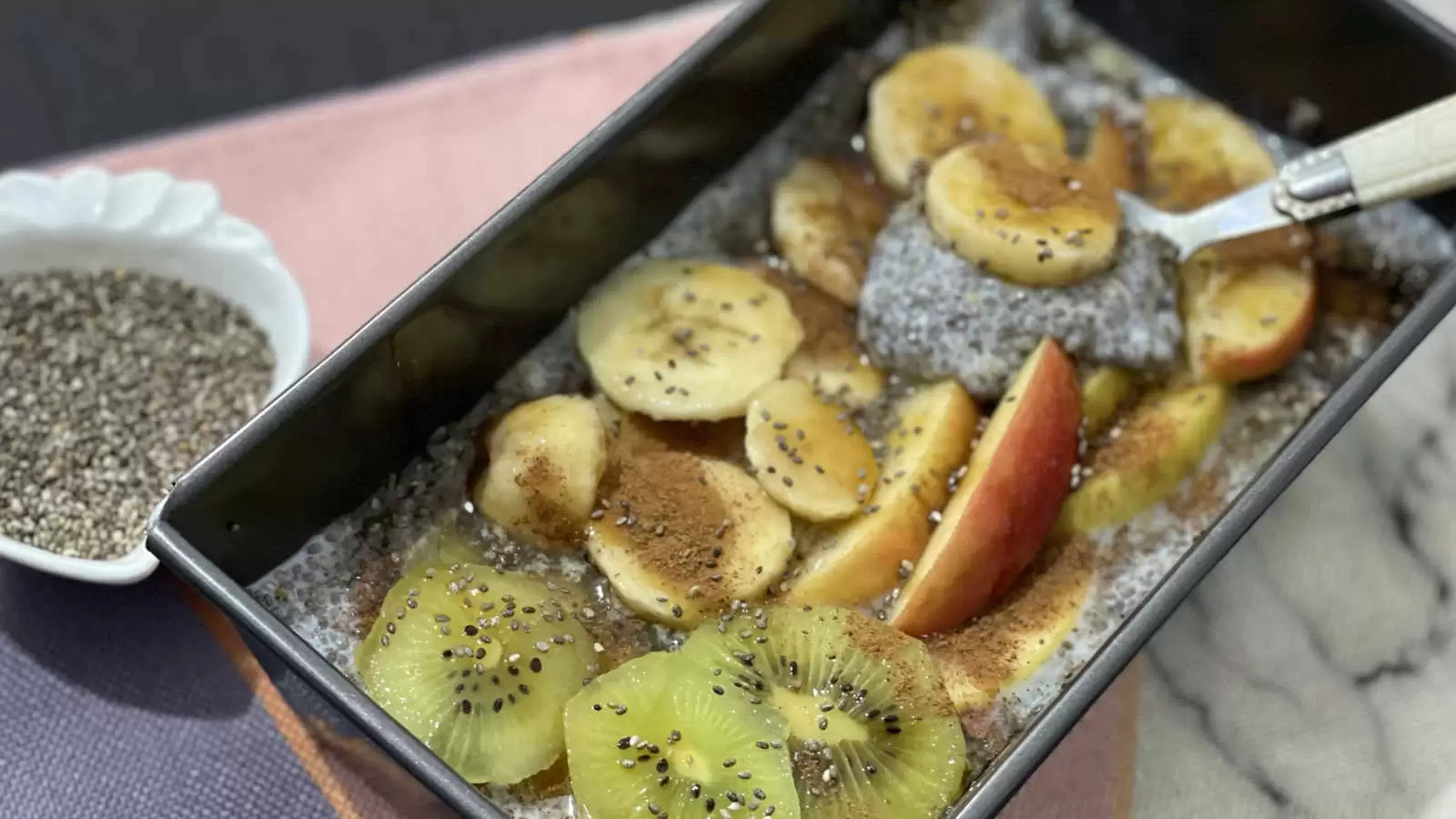 Chia pudding dish in a mold tablespoon apple banana and cut kiwi bowl with chia seeds napkin underneath