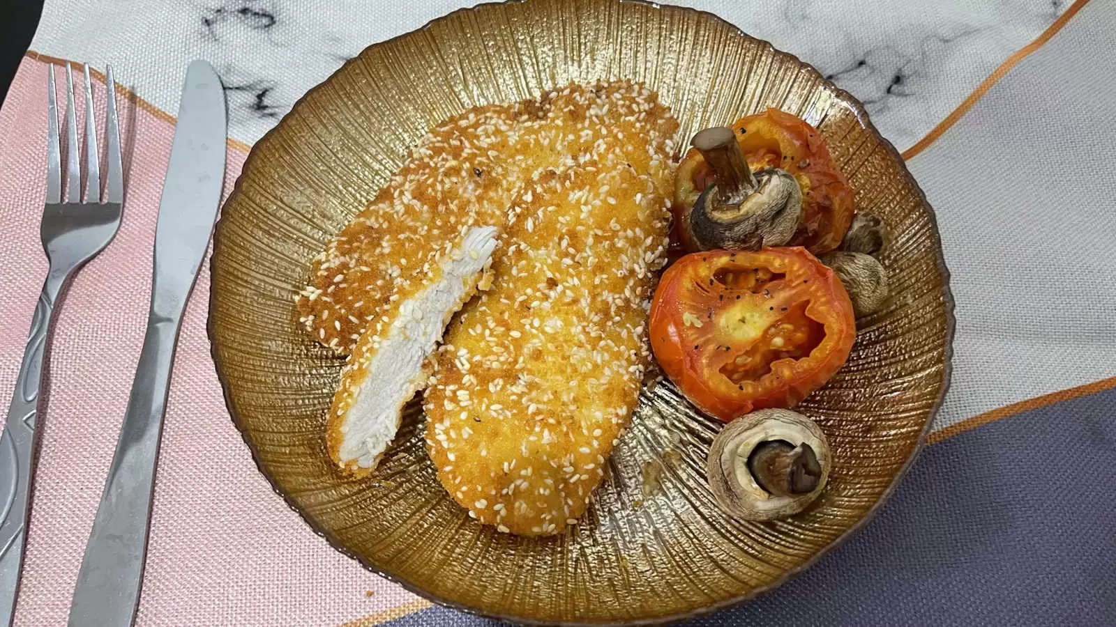 Chicken Schnitzel recipe roasted tomatoes and mushrooms on a gold colored plate on a napkin and a fork and knife on the side