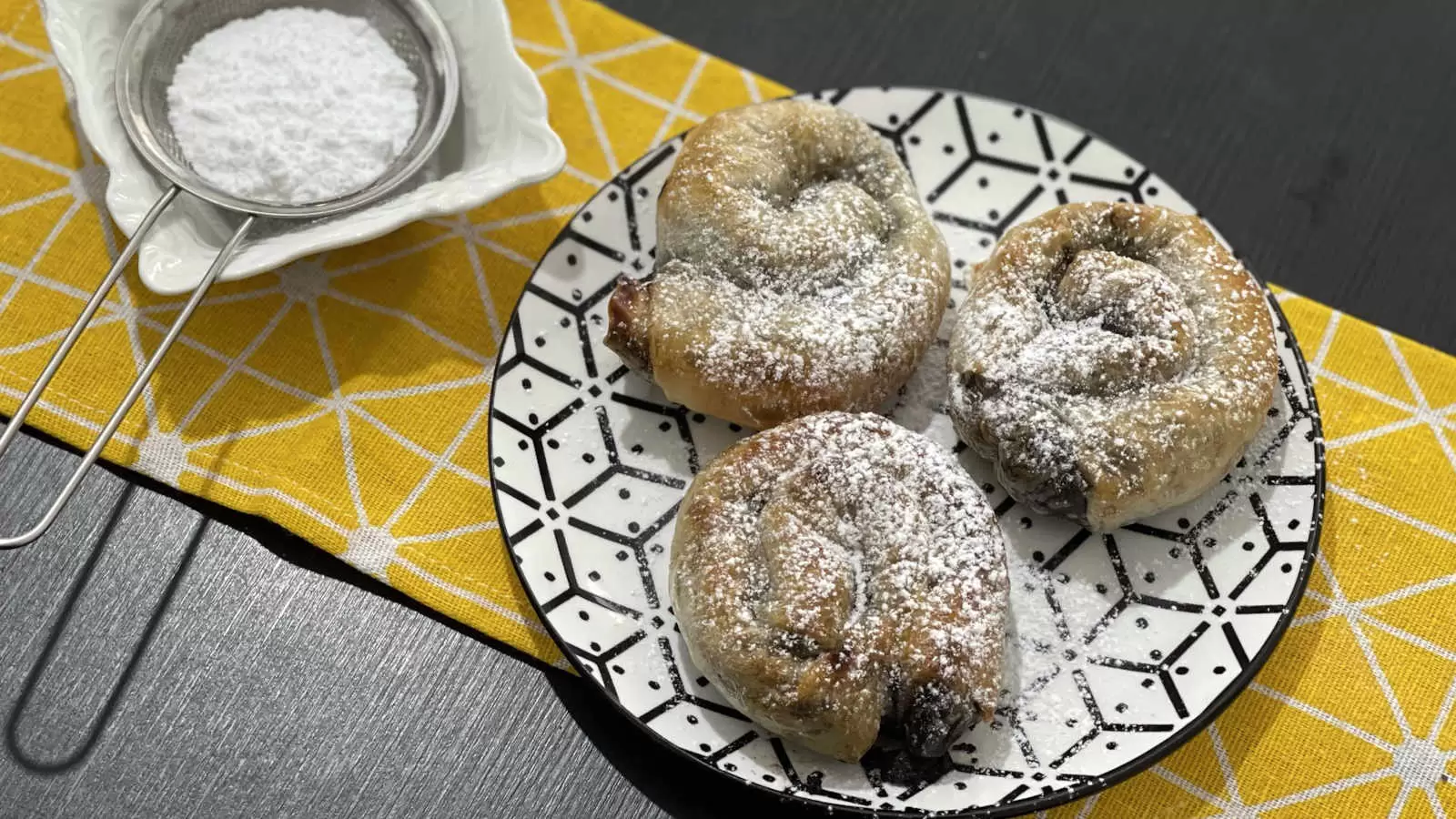 Three Chocolate rice paper on a plate a bowl with powdered sugar under a yellow napkin on the table