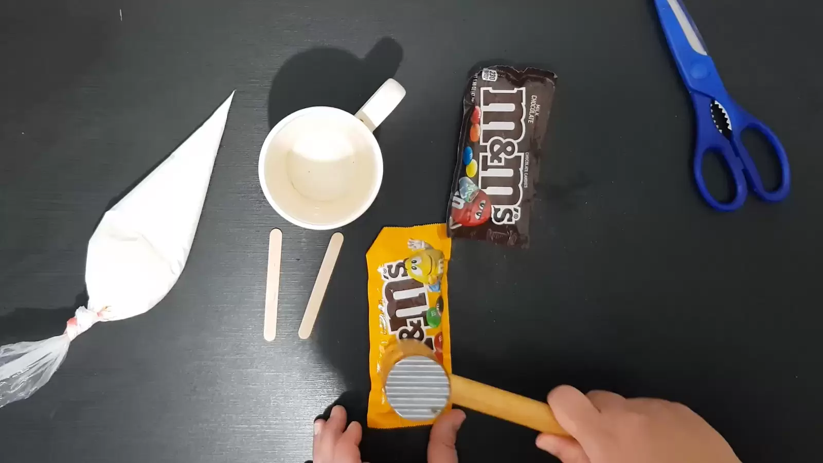 2 bags of M&M\\'s, kitchen hammer, scissors, cup and popsicle sticks, whipping cream