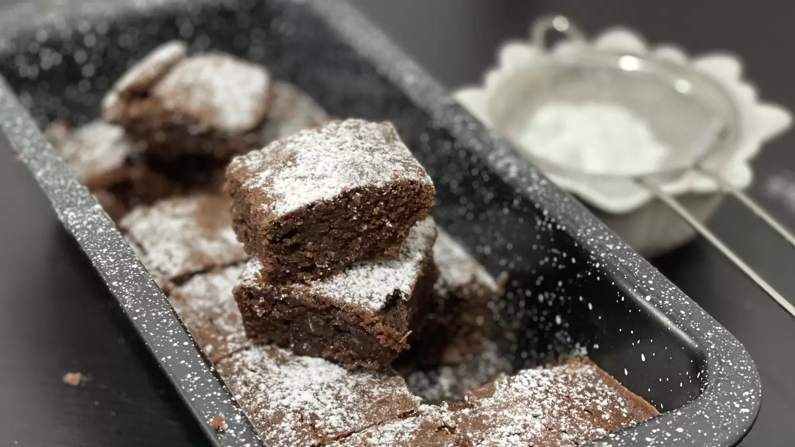 Brownies delicious in a pan brownie pieces one on top of the other next to powdered sugar in a bowl