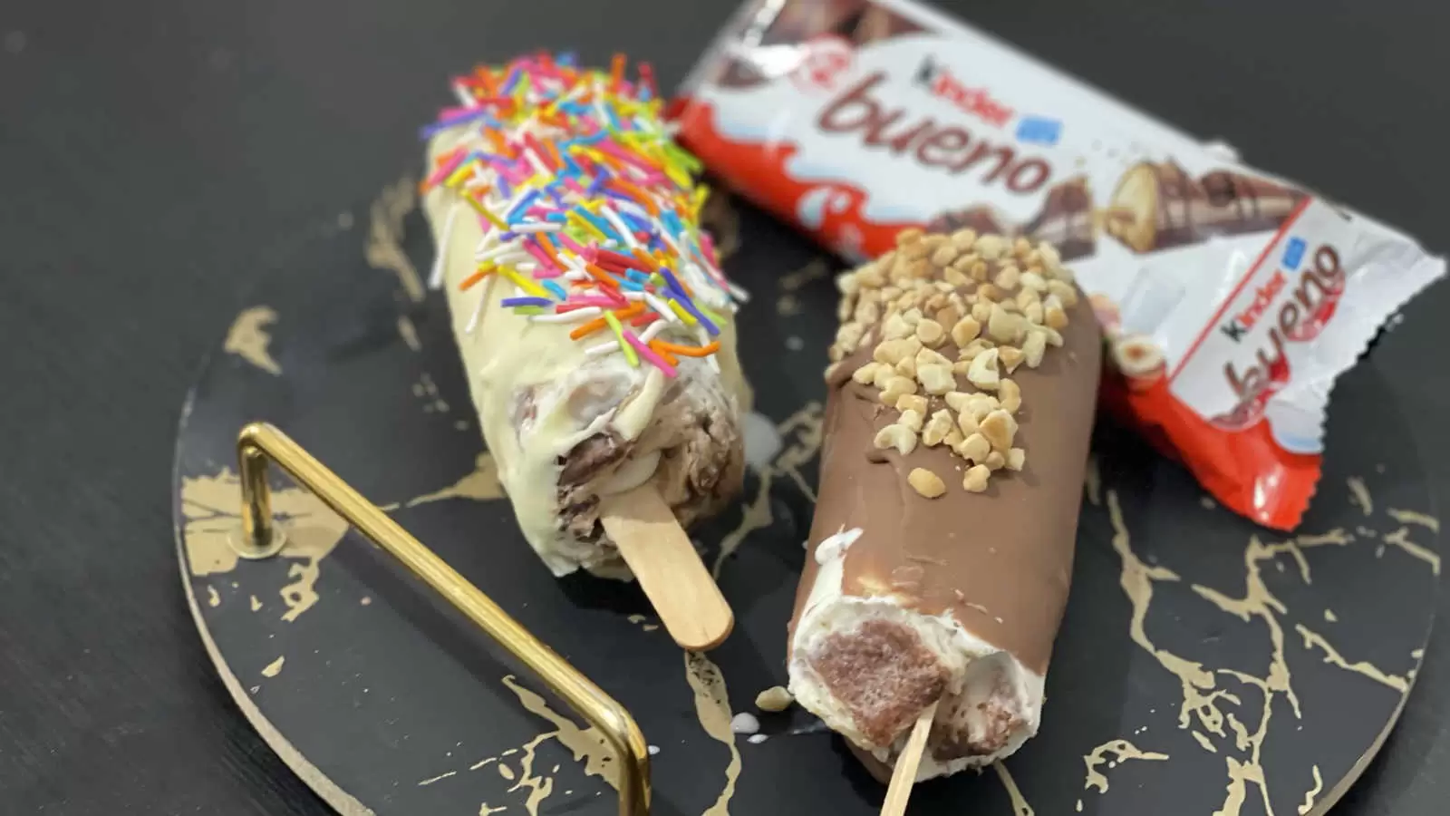 2 Kinder Bueno ice creams on a tray a Kinder Bueno chocolate bar on a black table