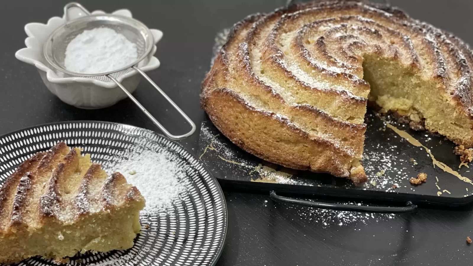 Delicious Orange and almond cake on a tray a slice of cake cut on the side there is a bowl with powdered sugar