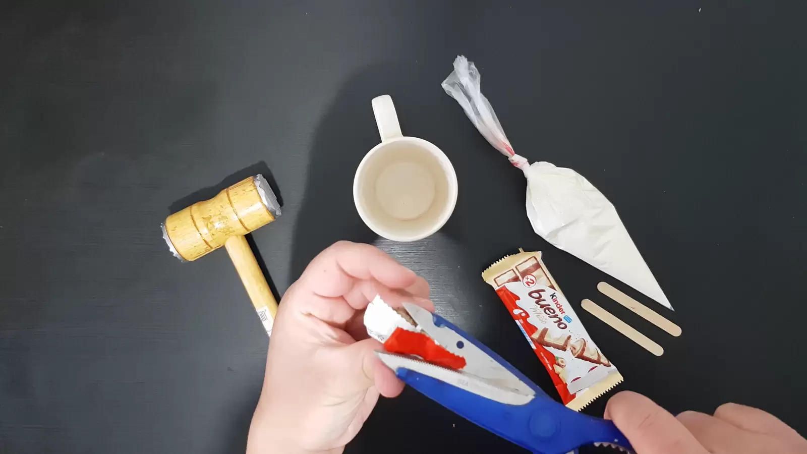 Whipped cream, a cup, Kinder Bueno, two wooden sticks, scissors and a kitchen hammer