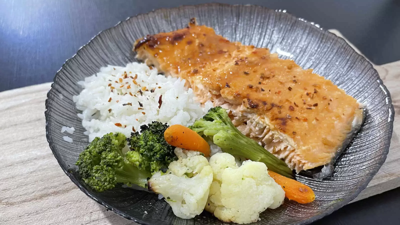 Healthy Honey Glazed Salmon rice carrots broccoli and cauliflower on a black plate on a wooden board