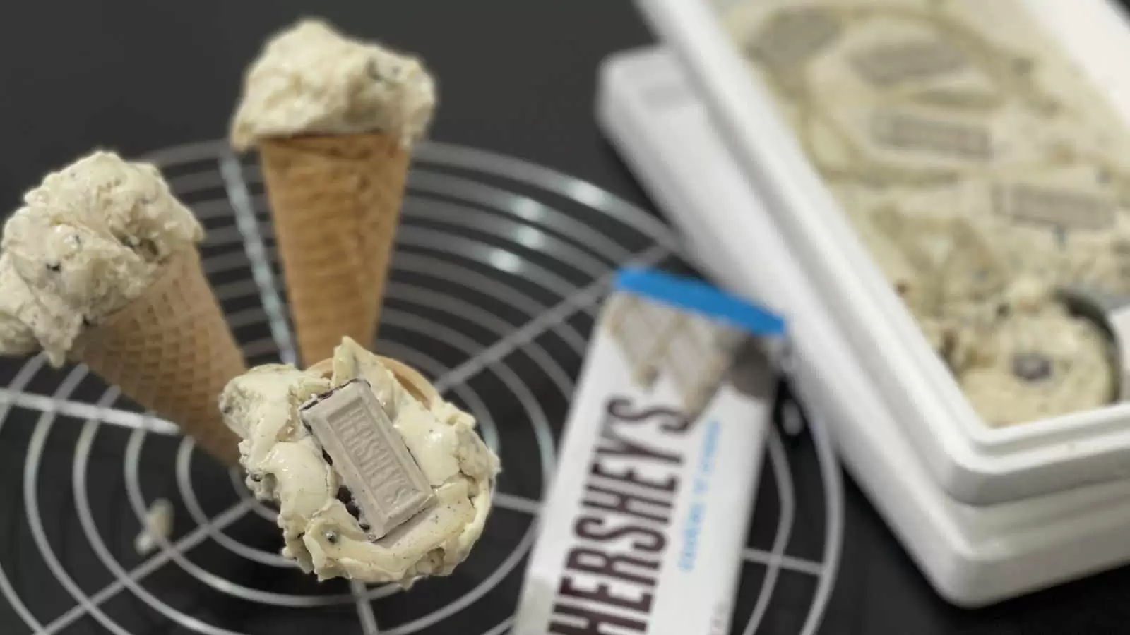 Hersheys ice cream recipe in a box with an ice cream scoop a cooling rack with three ice cream cones a pack of Hersheys chocolat