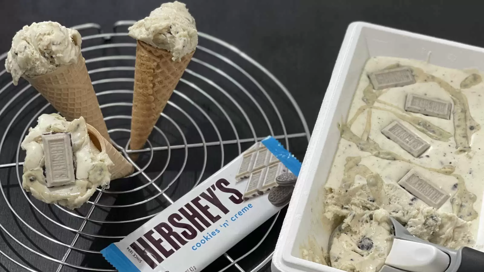 Homemade Hersheys ice cream in a box with an ice cream scoop a cooling rack with three ice cream cones a pack of Hersheys chocolate