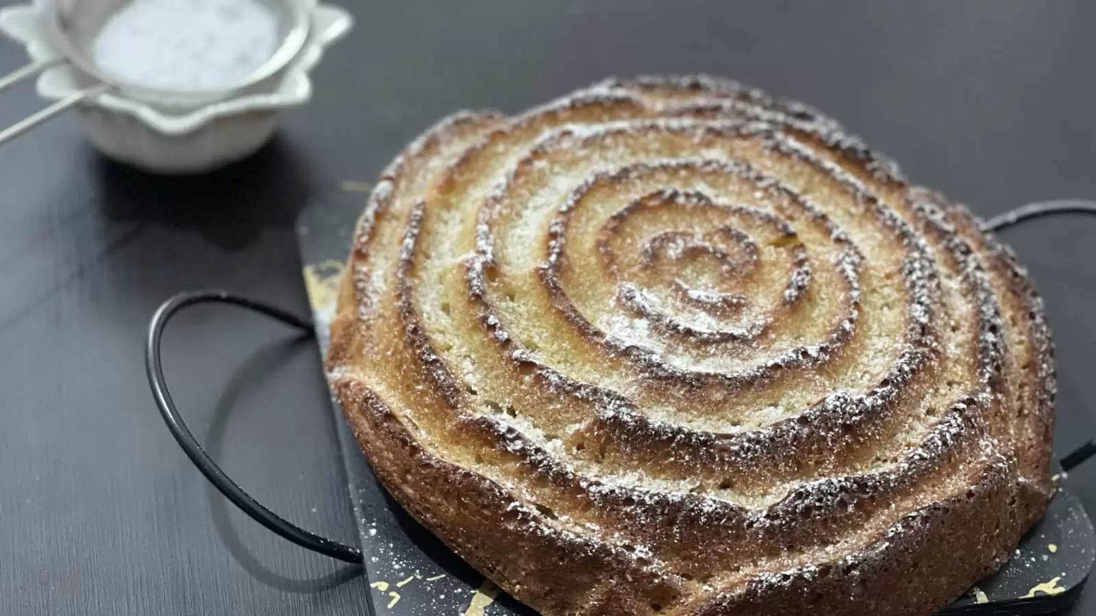 homemade Orange and almond cake on a tray a slice of cake cut on the side there is a bowl with powdered sugar