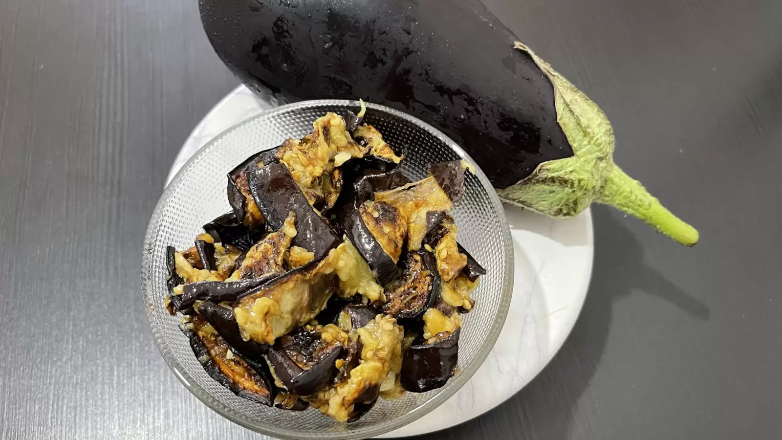 Eggplant and homemade eggplant salad next to it in a bowl on a tray on the table