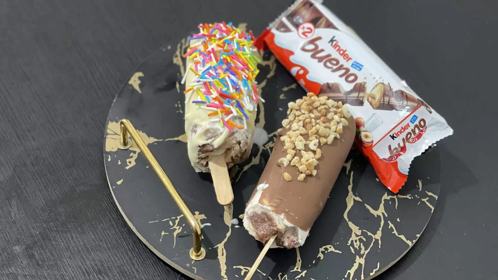 2 Kinder Bueno ice creams on a tray a Kinder Bueno chocolate bar on a black table