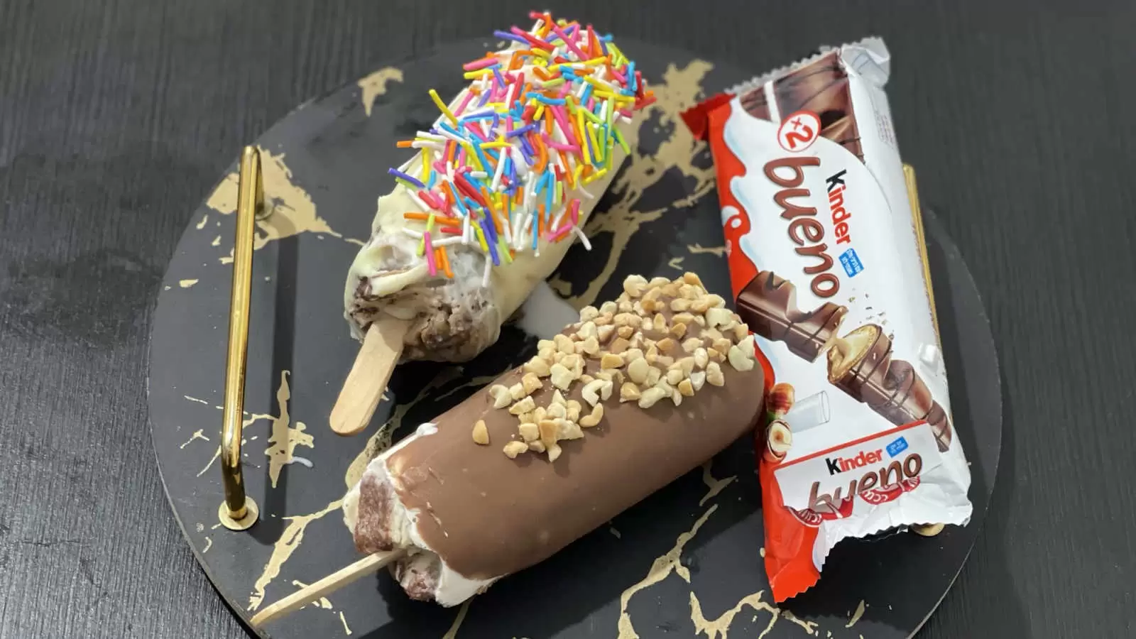 2 Kinder Bueno ice creams dish on a tray a Kinder Bueno chocolate bar on a black table