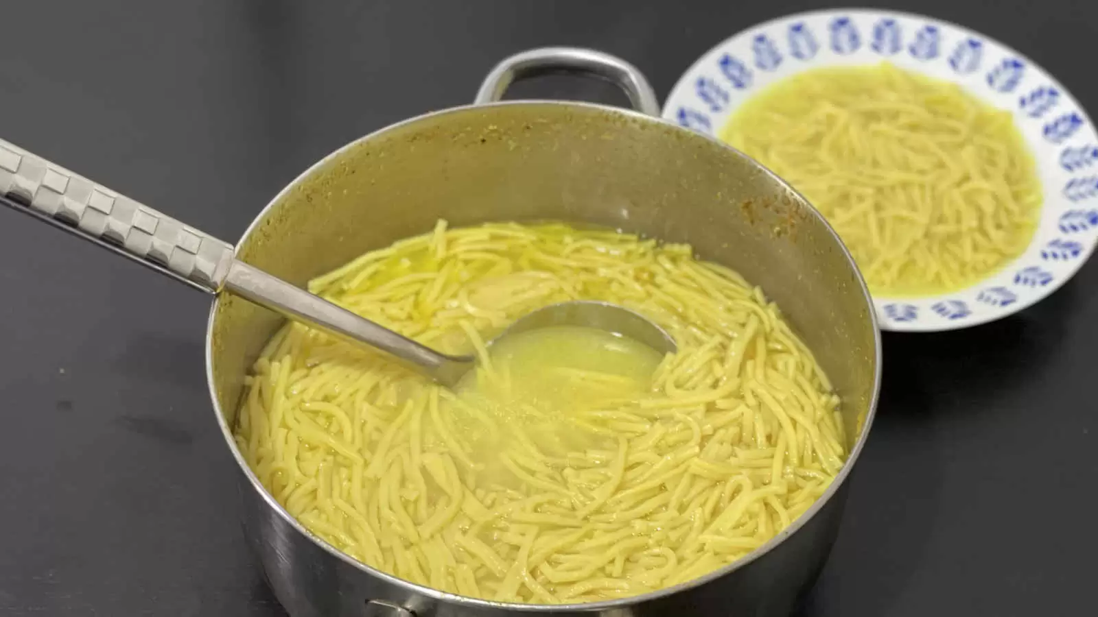 A plate with a dish of noodles a ladle in a pot with noodle soup