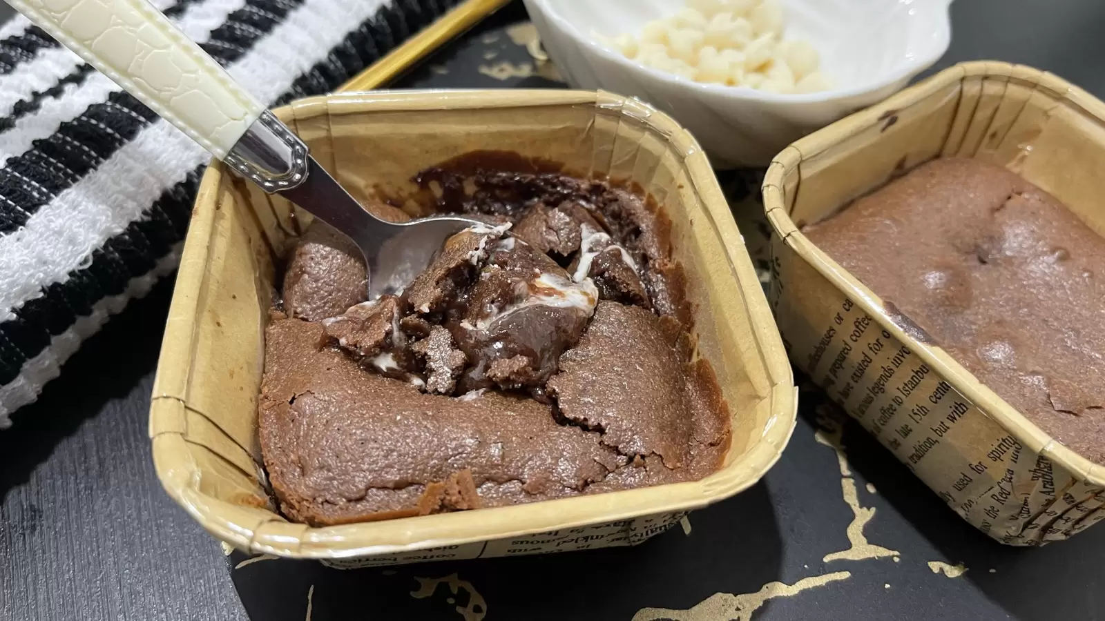 Two Nutella souffls Dessert on a tray one with a spoon a bowl with white chocolate and a towel on the side
