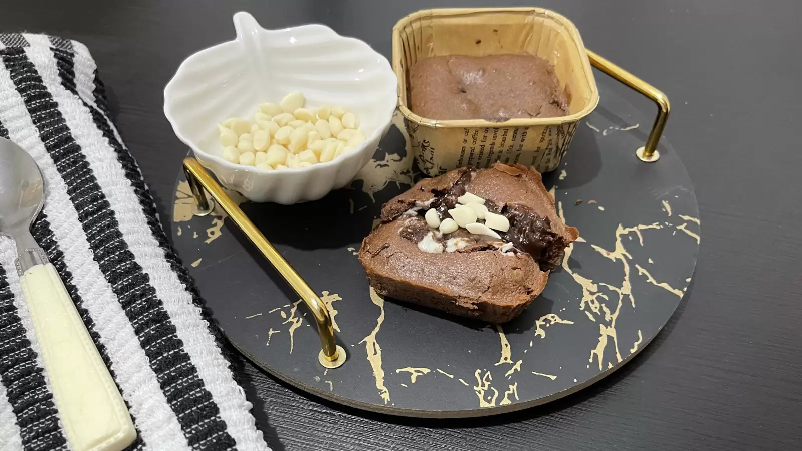 Two Nutella souffls on a tray with a spoon a bowl with white chocolate and a towel on the side