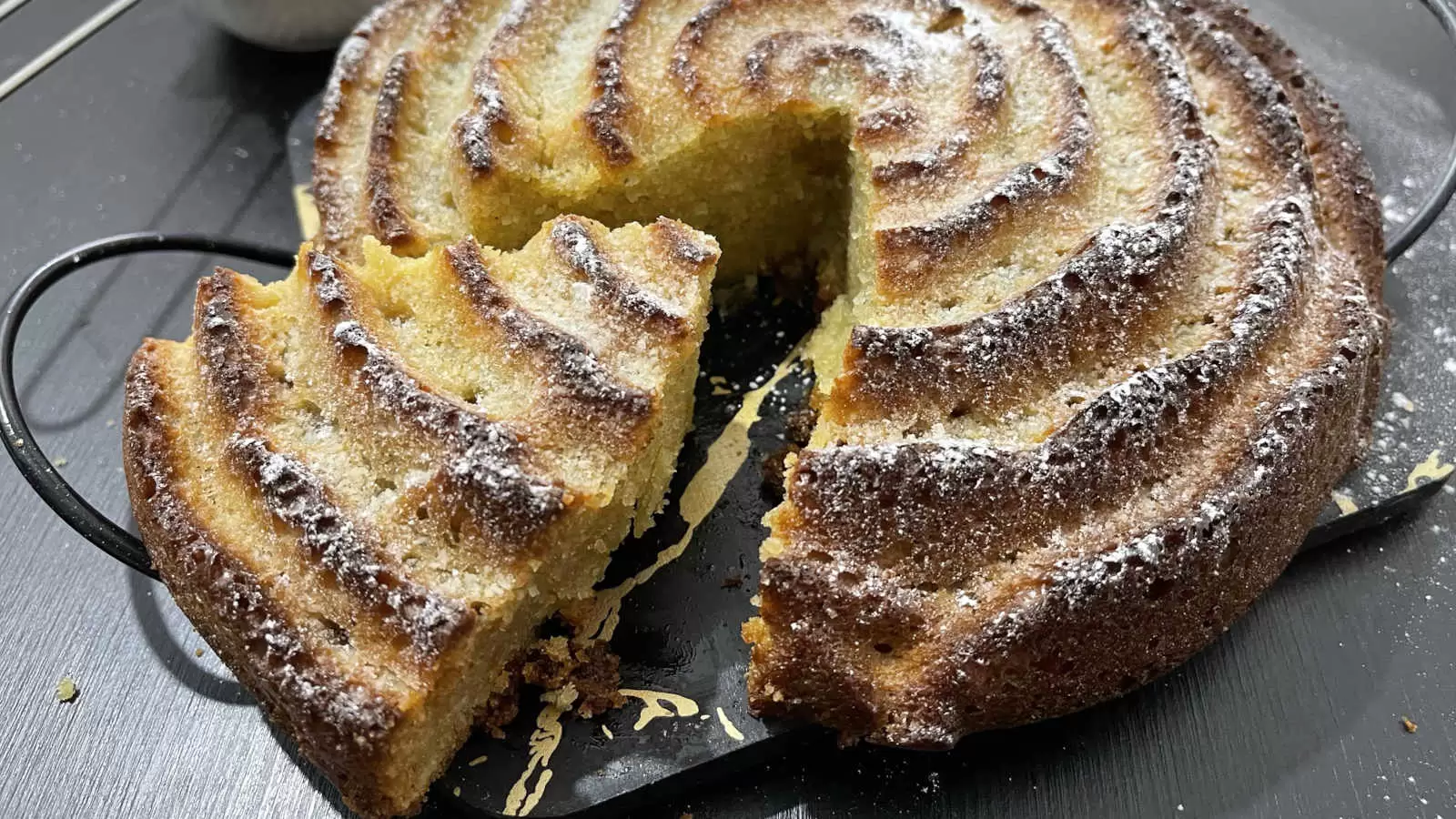 Orange and almond cake recipe on a tray a slice of cake cut on the side there is a bowl with powdered sugar