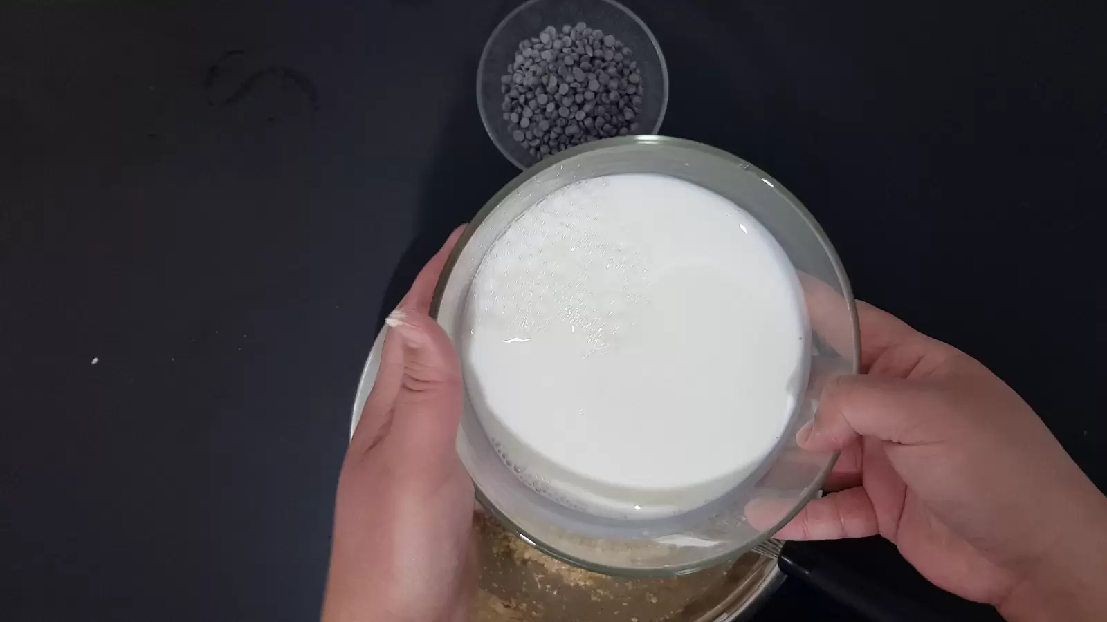 A bowl with chocolate chips, a bowl with milk, a whisk, a mixture in a bowl