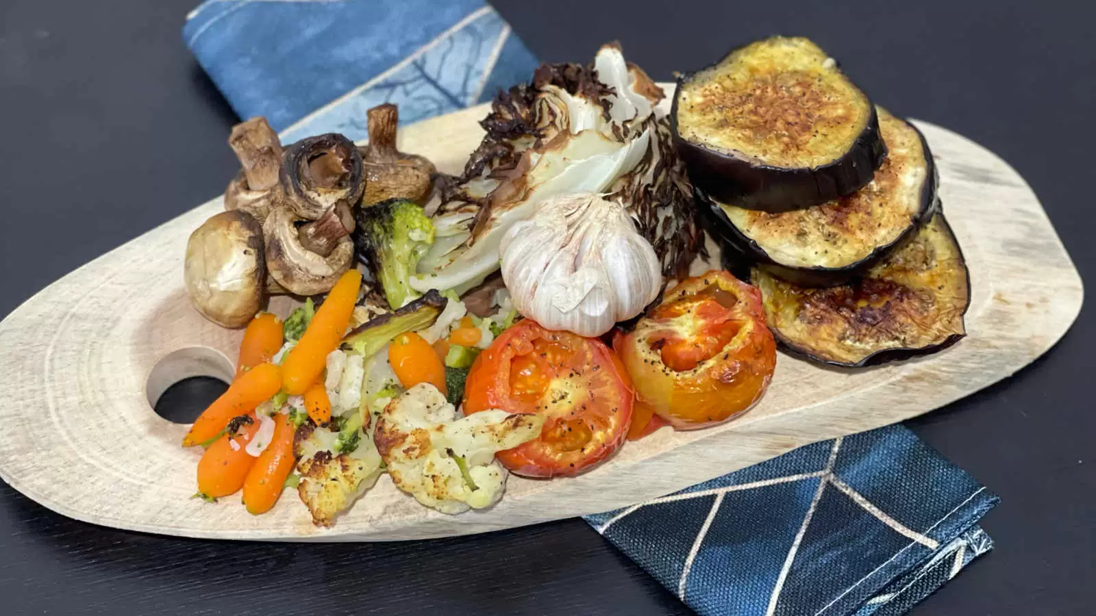 Eggplant mushrooms tomatoes cabbage carrots and other roasted vegetables on a wooden tray