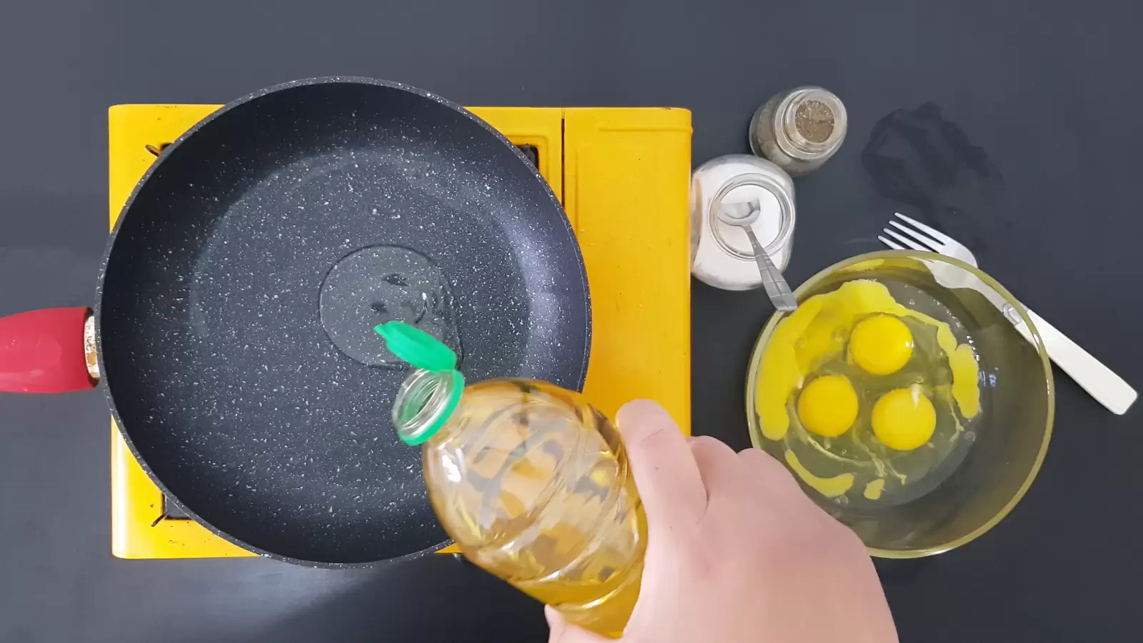 4 eggs in a bowl, a fork, a jar of salt, a jar of pepper, a pan with oil