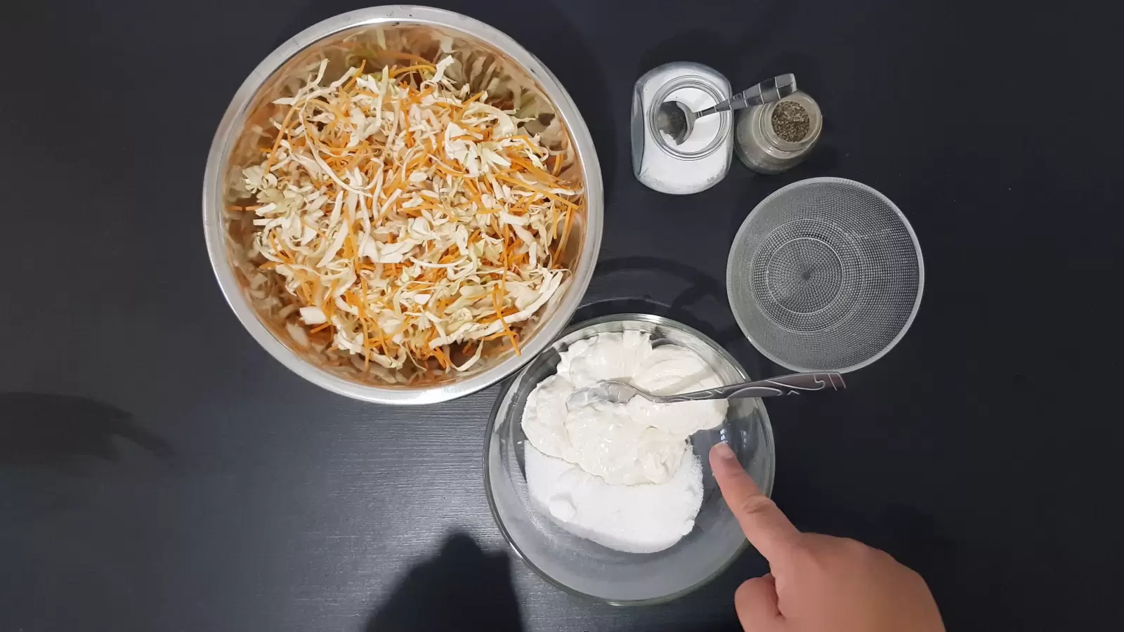 One bowl with cut carrots and cabbage, a second bowl with mayonnaise and sugar, a bowl with vinegar, salt and pepper in a jar