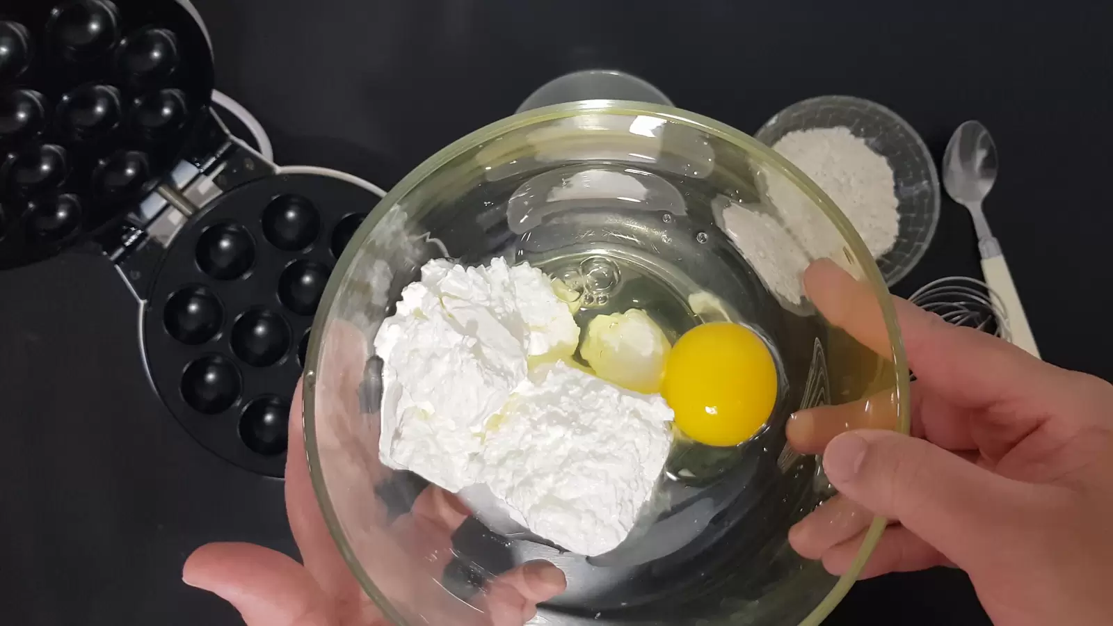 Cheese and egg in a bowl, a bowl with flour, a spoon, a device for making pancake balls