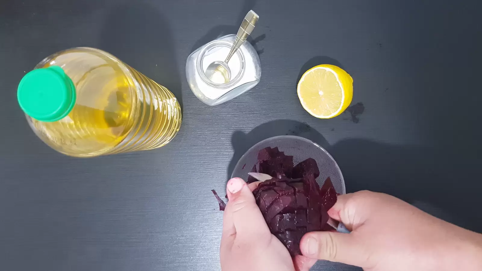 Half a lemon, a jar of salt with a spoon, a bottle of olive oil, a bowl of beets and a knife