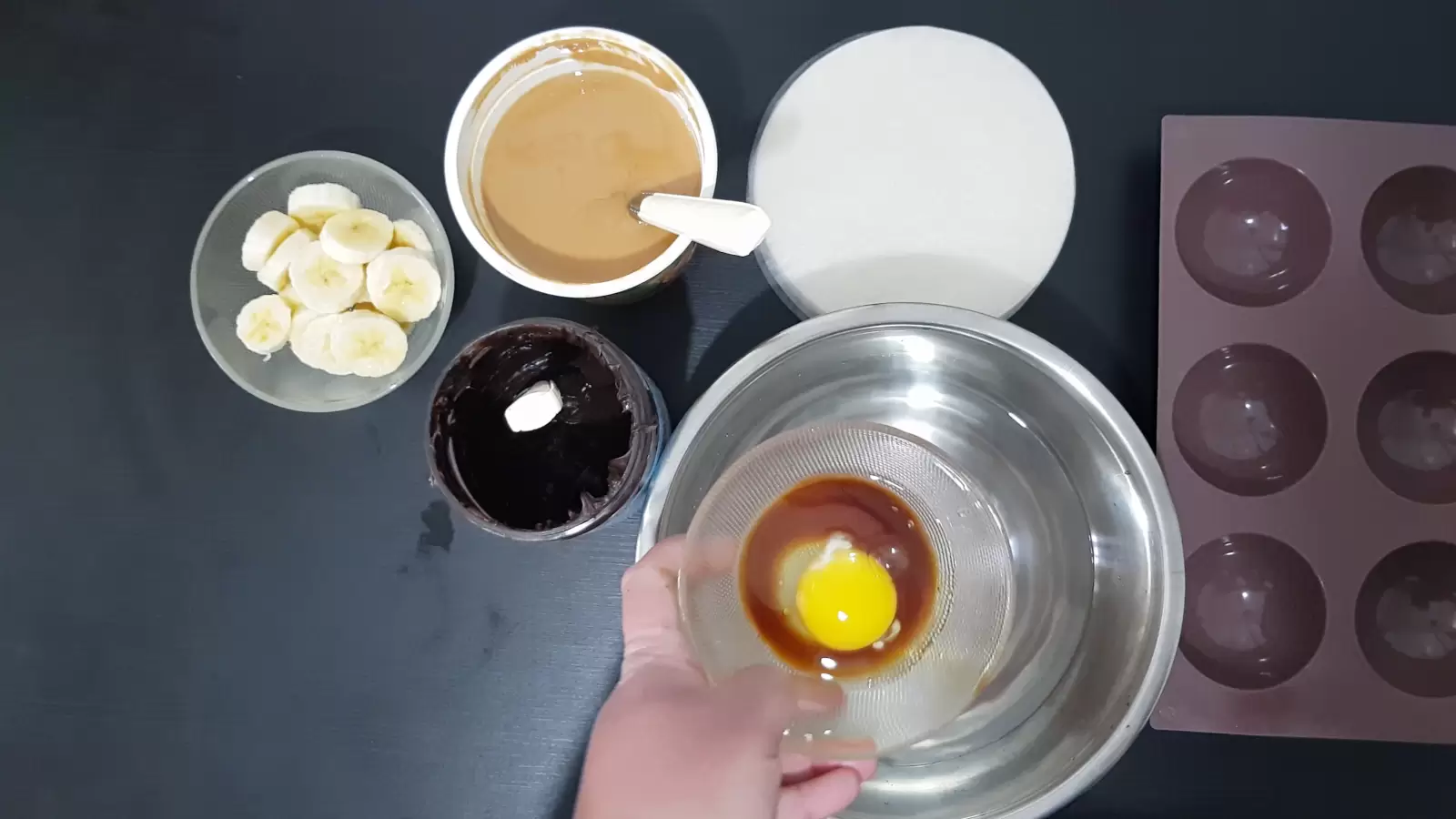 Muffin pan, rice paper, peanut butter jar, chocolate jar, bowl of sliced ​​bananas, large bowl of water, and large bowl of date sauce and egg