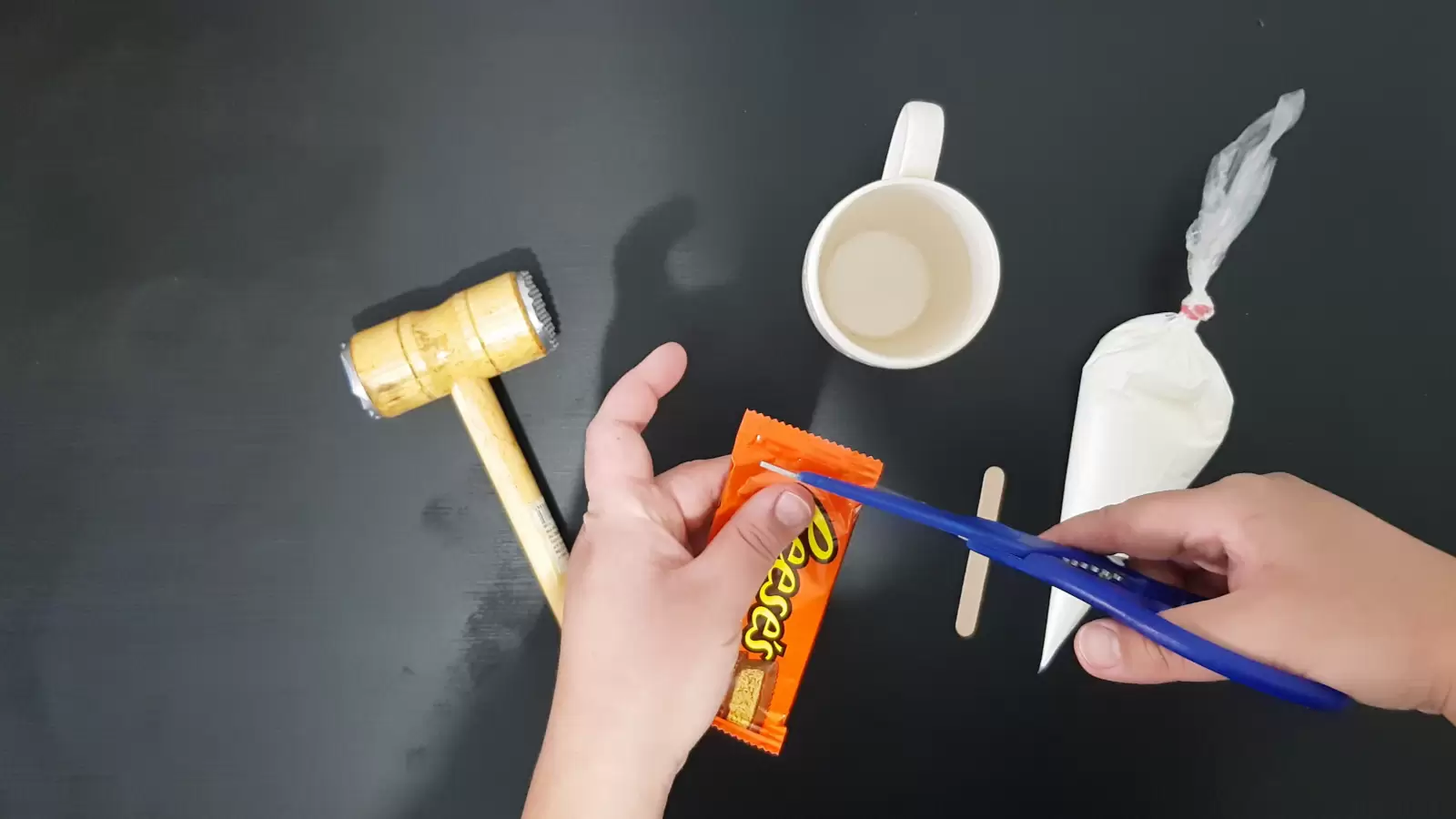 Sweet cream in a piping bag, mug, kitchen hammer, popsicle stick, scissors cutting a Reeses package