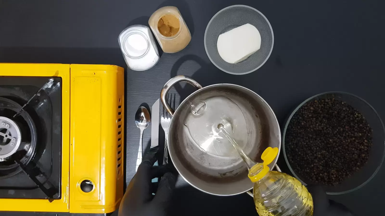 Bowl with lentils, bowl with half an onion, jar of cumin, jar of salt, gas jar, pot, bottle of oil spilled, knife and spoon