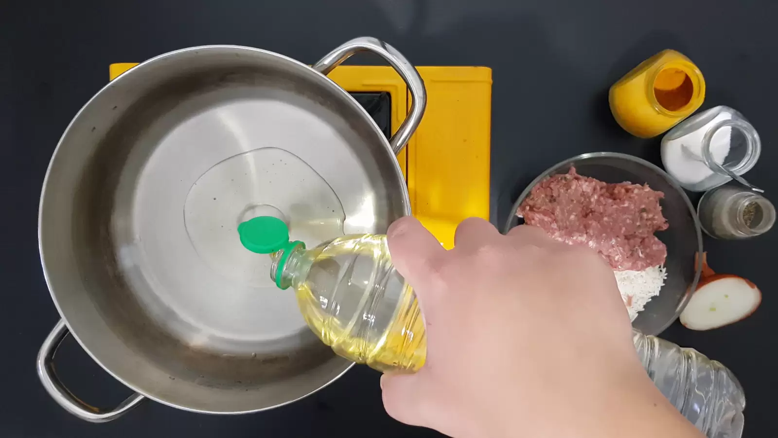 Jar with turmeric, jar with salt, jar with black pepper, half an onion, bowl with minced meat and rice, oil poured into a pot