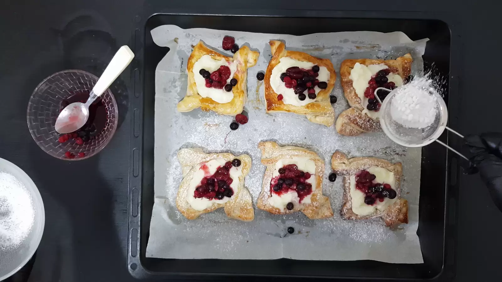 Powdered sugar on Danish pastry ready on a baking sheet, bowl with empty spoon