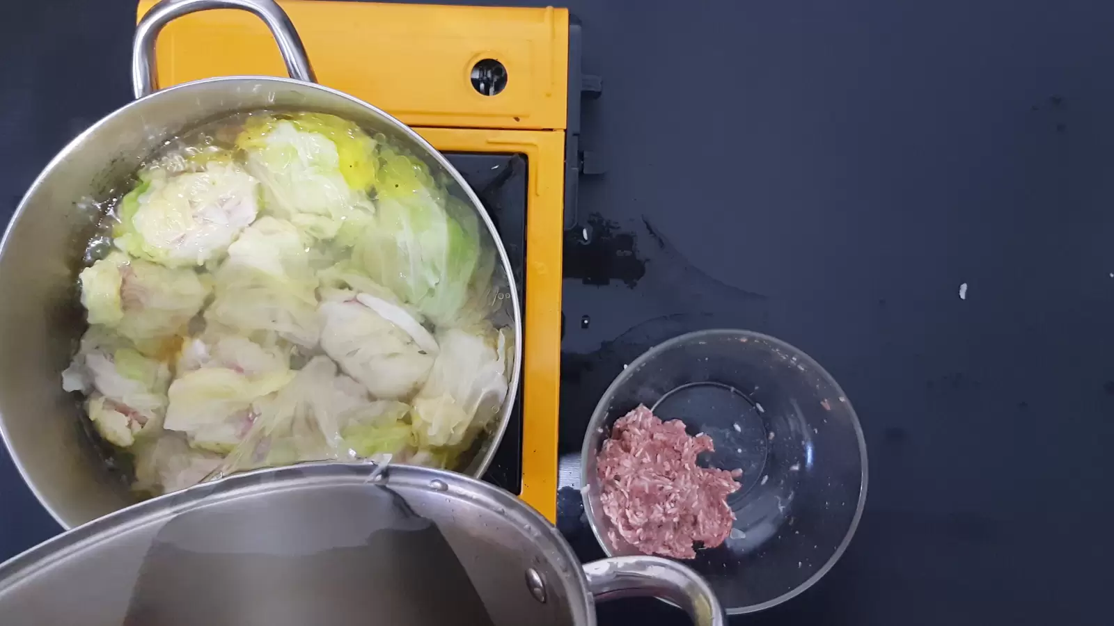 A pot with stuffed cabbage leaves, a pot with water, a bowl with ground meat