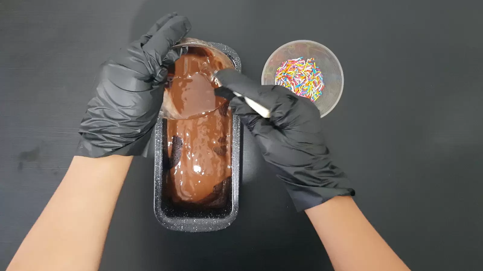 Bowl with sprinkles, English cake pan with chocolate cake, chocolate icing spread on top