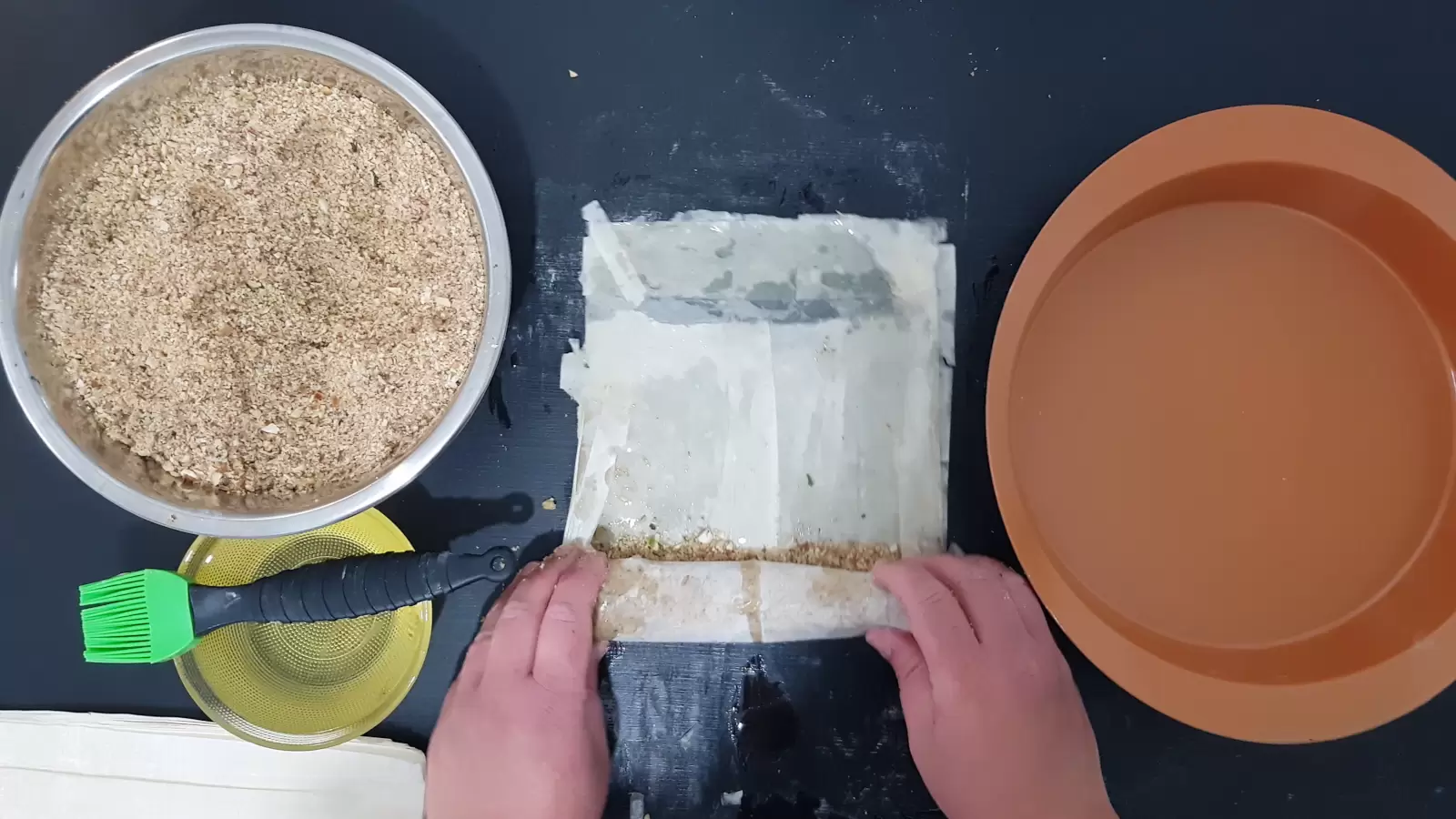 A mold for the oven, sheets of phyllo with the rolled nut mixture, a bowl with oil and a brush for spreading, a bowl with a mixture of chopped nuts