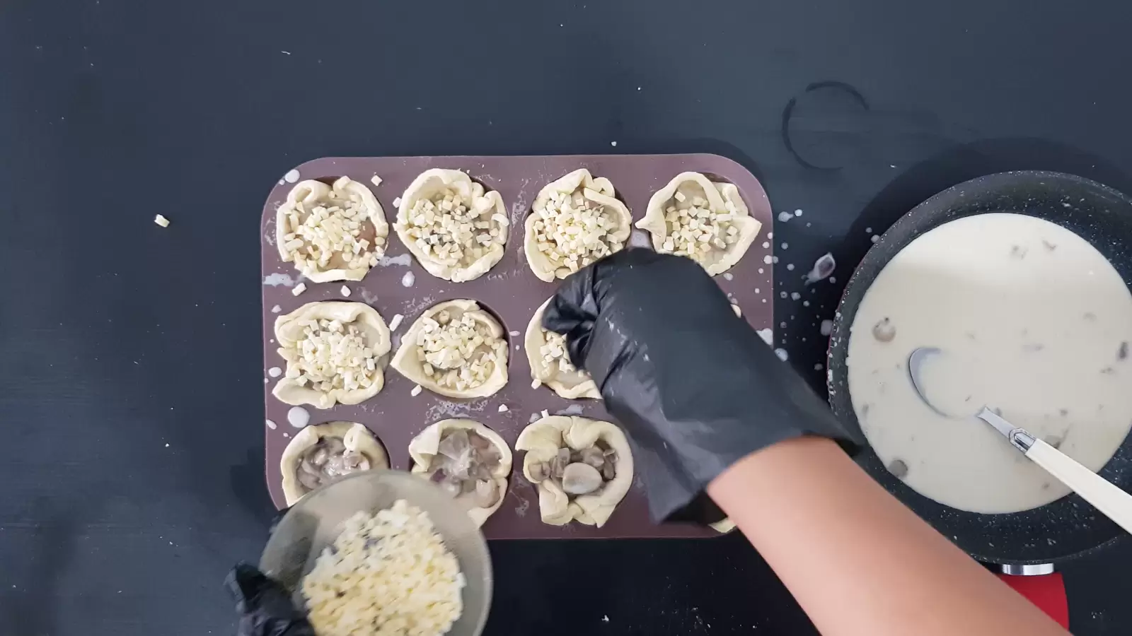 Pan with mushroom and cream filling, bowl with grated cheese over a springform pan with puff pastry squares