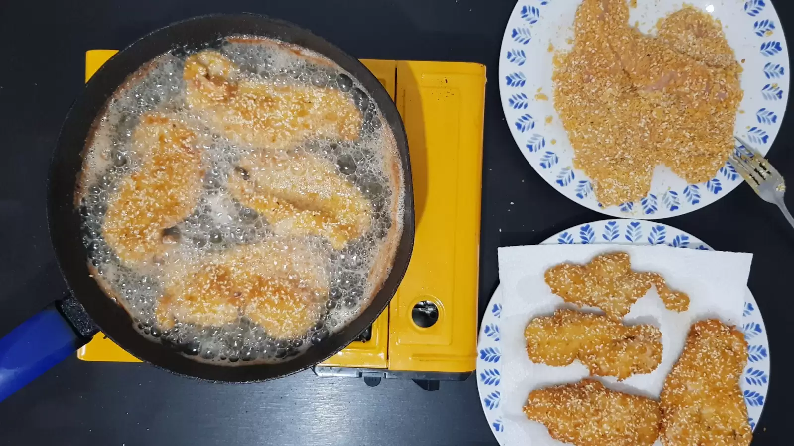 A plate with schnitzels and a fork, a pan with oil and schnitzels, a plate with absorbent paper and schnitzels on them