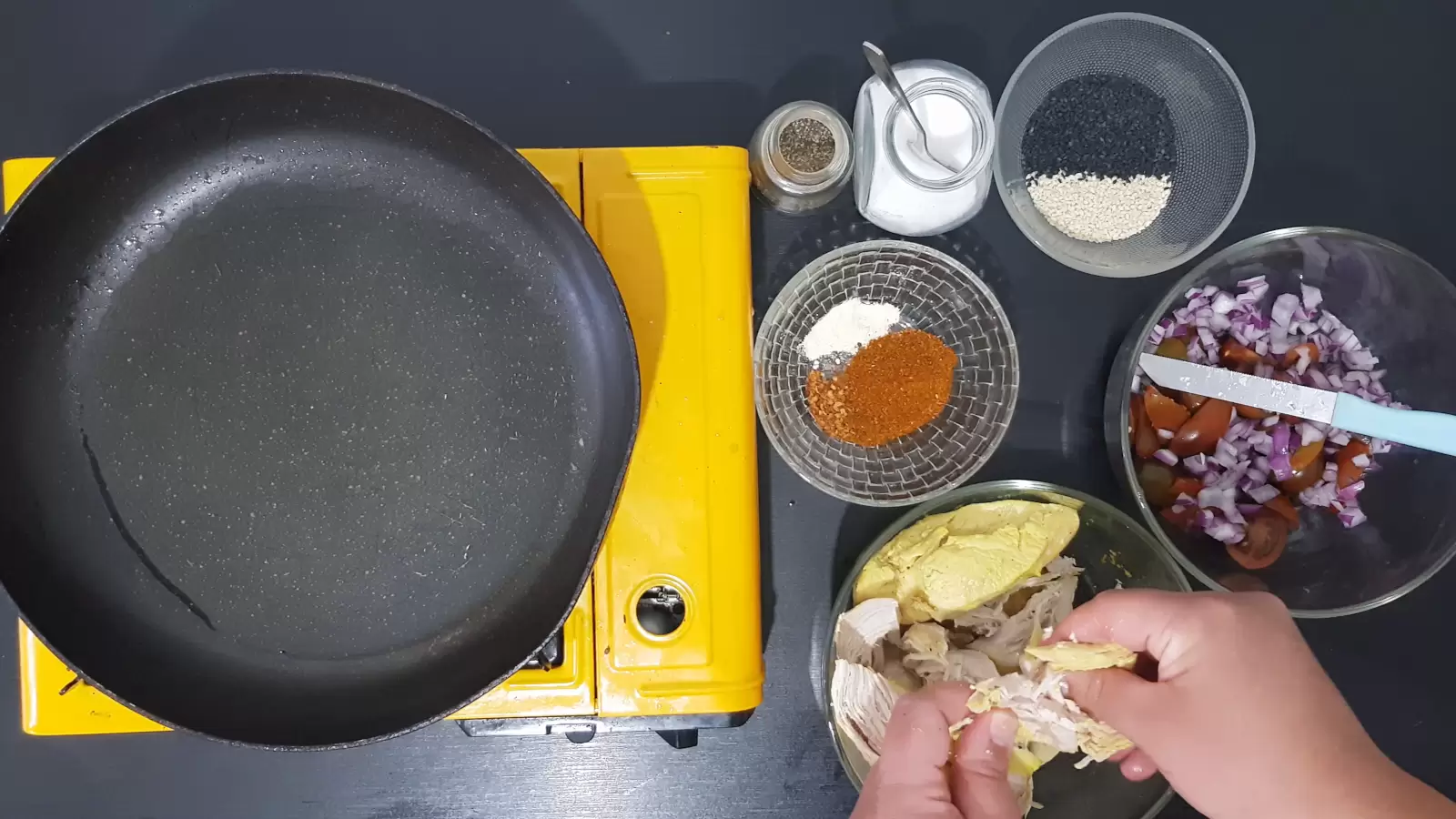 Spices, chicken sliced into strips, sesame, tomatoes, purple onion, frying pan