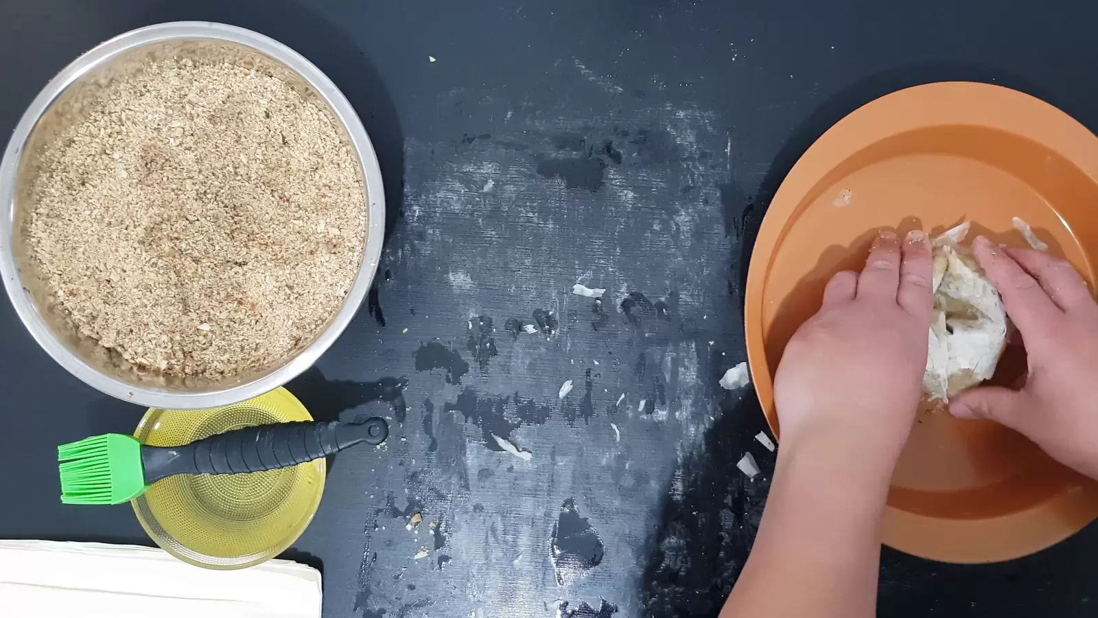 Sheets of phyllo with the nut mixture in an oven dish, a bowl with oil and a brush for spreading, a bowl with a mixture of chopped nuts