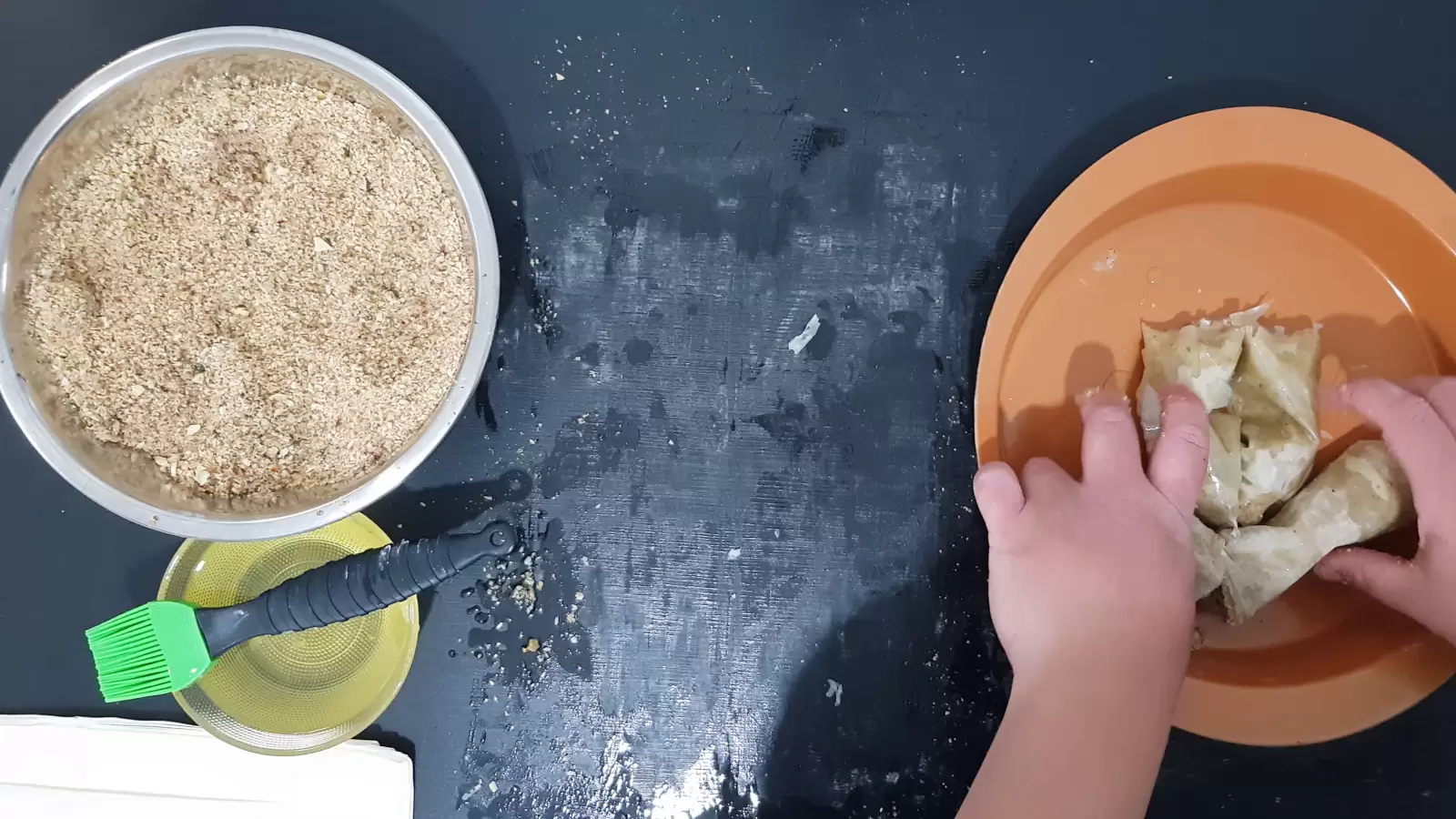 Sheets of phyllo with the nut mixture in an oven dish, a bowl with oil and a brush for spreading, a bowl with a mixture of chopped nuts