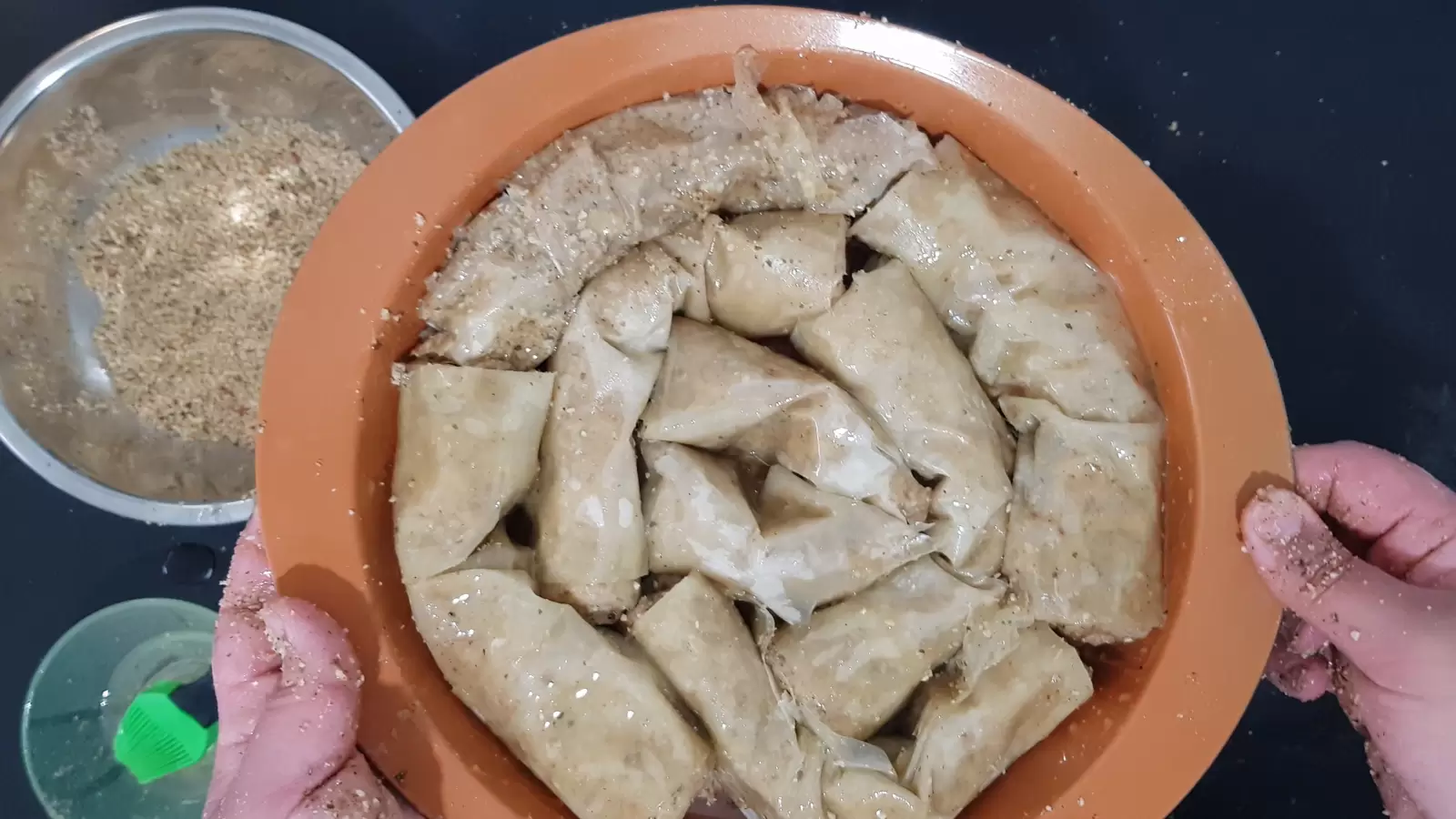 A mold with phyllo sheets, baklava, a bowl with a mixture of nuts, a bowl with oil and a brush for spreading