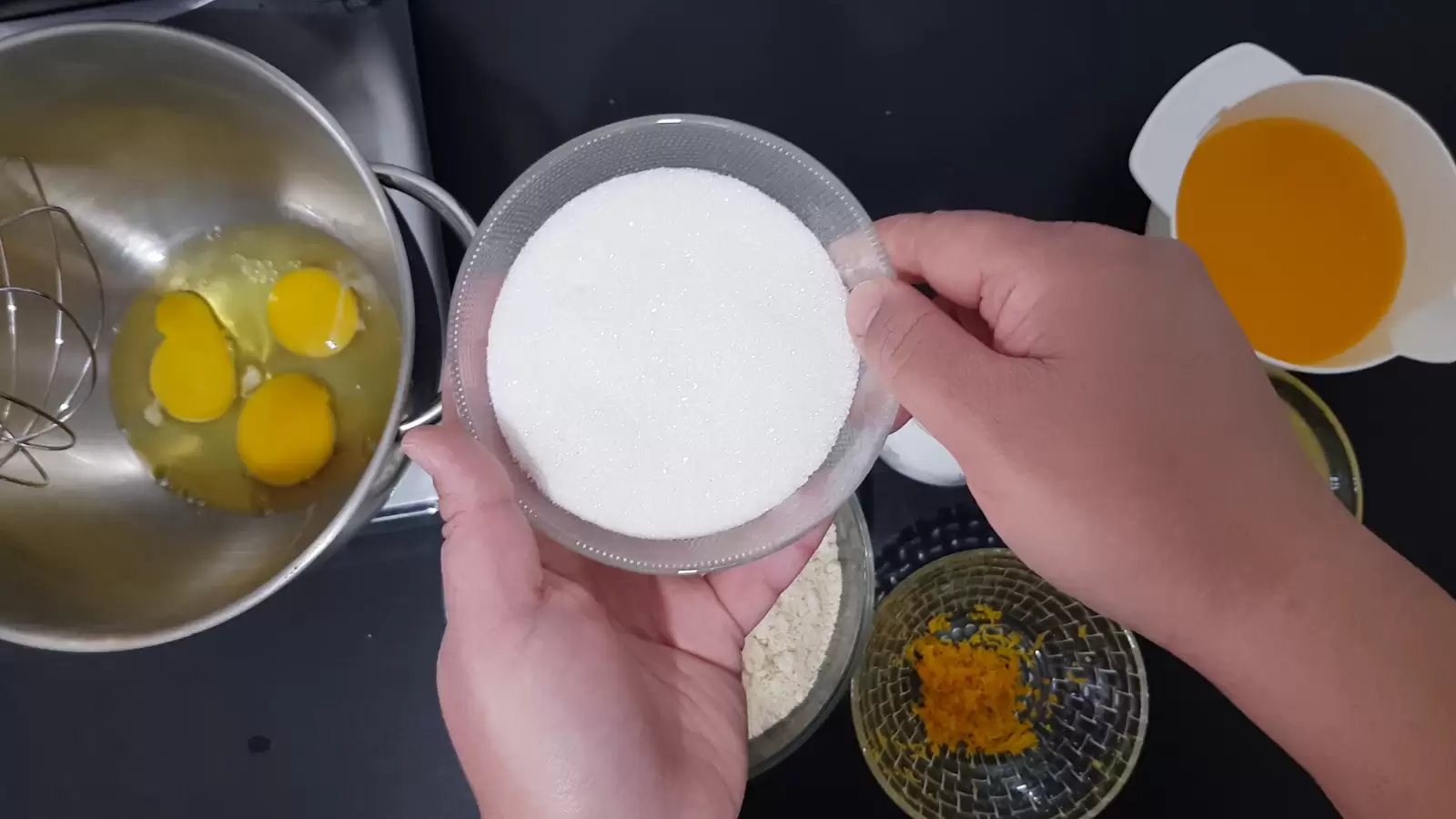 Three eggs in mixer bowl, bowl with sugar, bowl with orange zest, bowl with orange juice